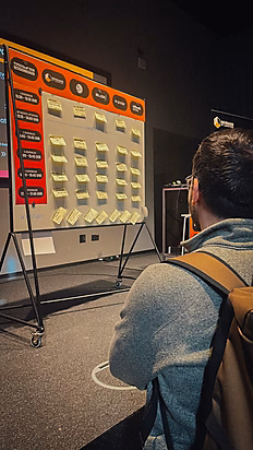Eine Person betrachtet ein großes Board mit Post-it-Zetteln, das auf einem Ständer steht, in einem Veranstaltungsraum.