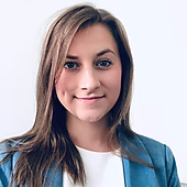 Porträt einer Frau mit langen braunen Haaren, die lächelt, in einem blauen Blazer vor einem hellen Hintergrund.